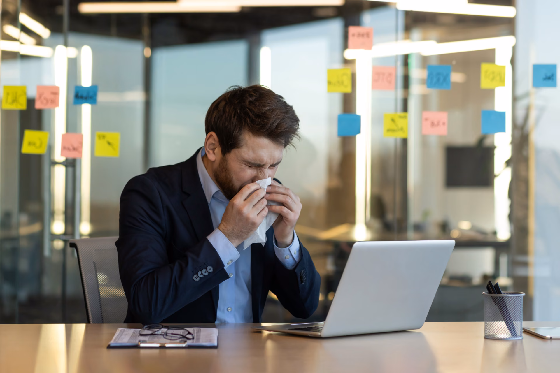 Sick office employee sneezing at his desk, illustrating the need for a workplace flu season disinfection cleaning plan