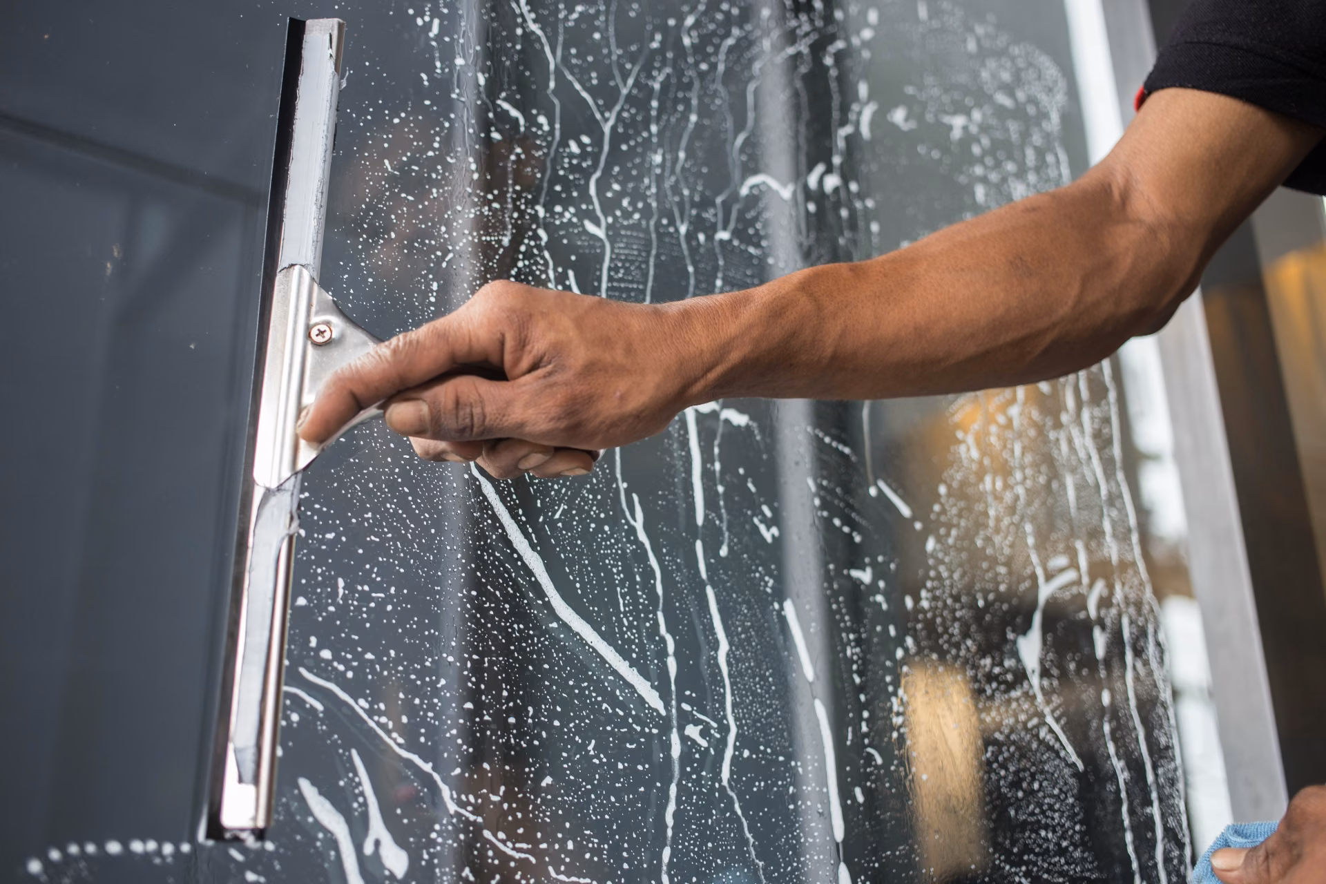 Professional cleaner using a squeegee to clean storefront entrance glass, protecting a retail store's first impression
